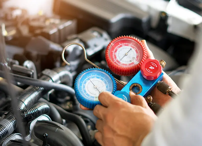 Technician checking a car's air conditioning system with manifold pressure gauges.