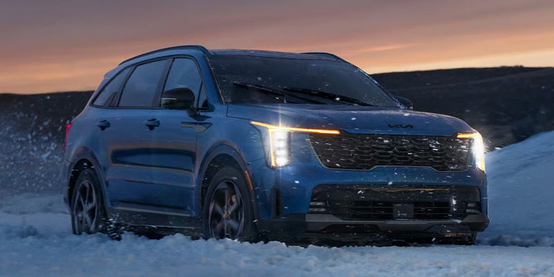Kia Sorento driving through snow at sunset.